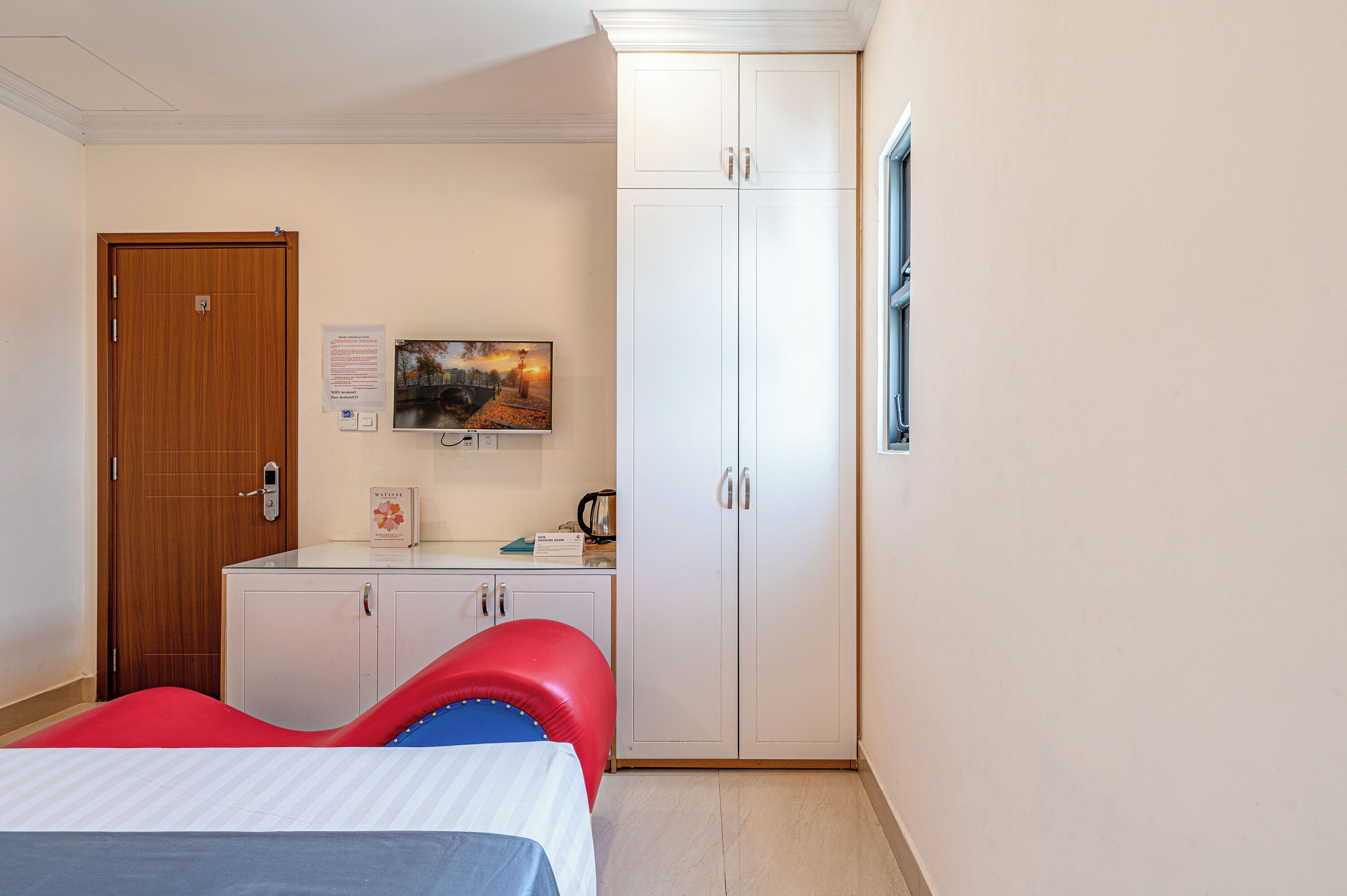 Una habitación de hotel con una cama, un escritorio con computadora, un armario y una ventana.