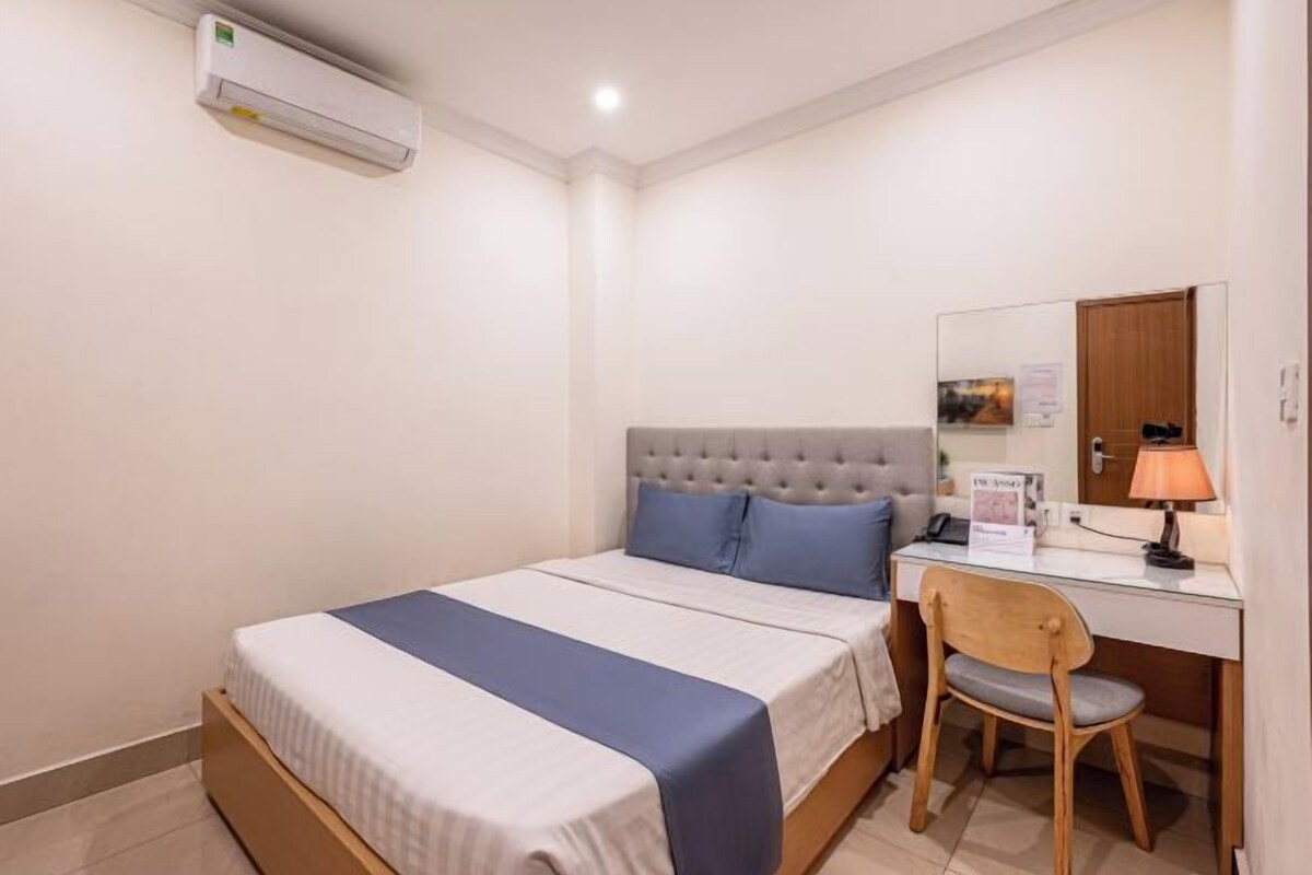 Una habitación de hotel con cama, escritorio, silla, espejo y unidad de aire acondicionado.