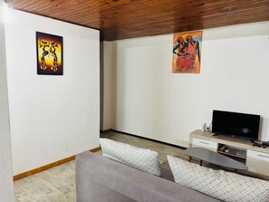 Ein Wohnzimmer mit einer Couch, einem Fernseher und zwei Kunstwerken an den Wänden.