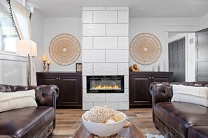 A living room with two leather sofas, a white fireplace, and decorative woven wall hangings.