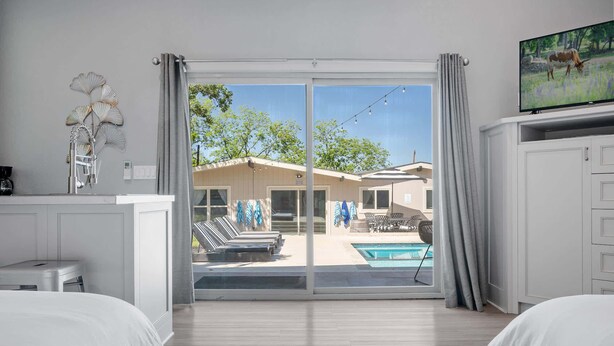 Habitación de hotel con cama, televisor, piscina y vistas al exterior.