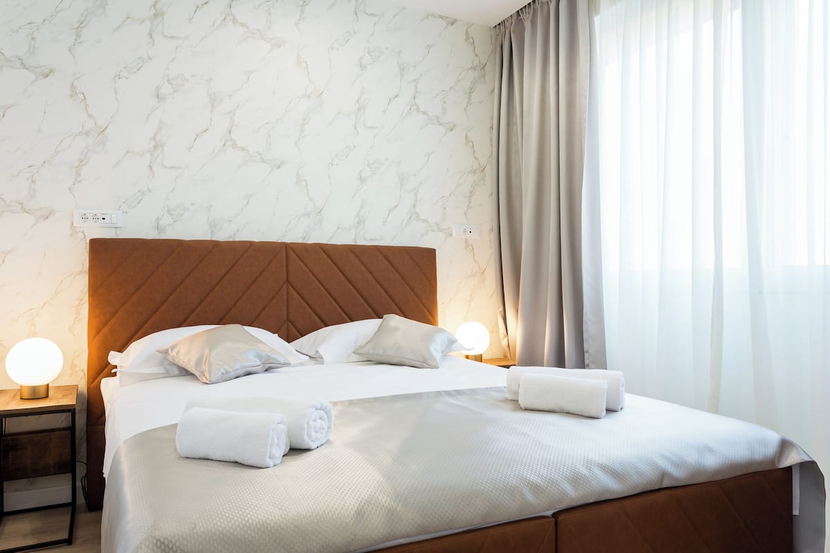 Un lit bien fait, avec du linge de lit blanc et deux oreillers, une tête de lit en bois et deux lampes de chevet.