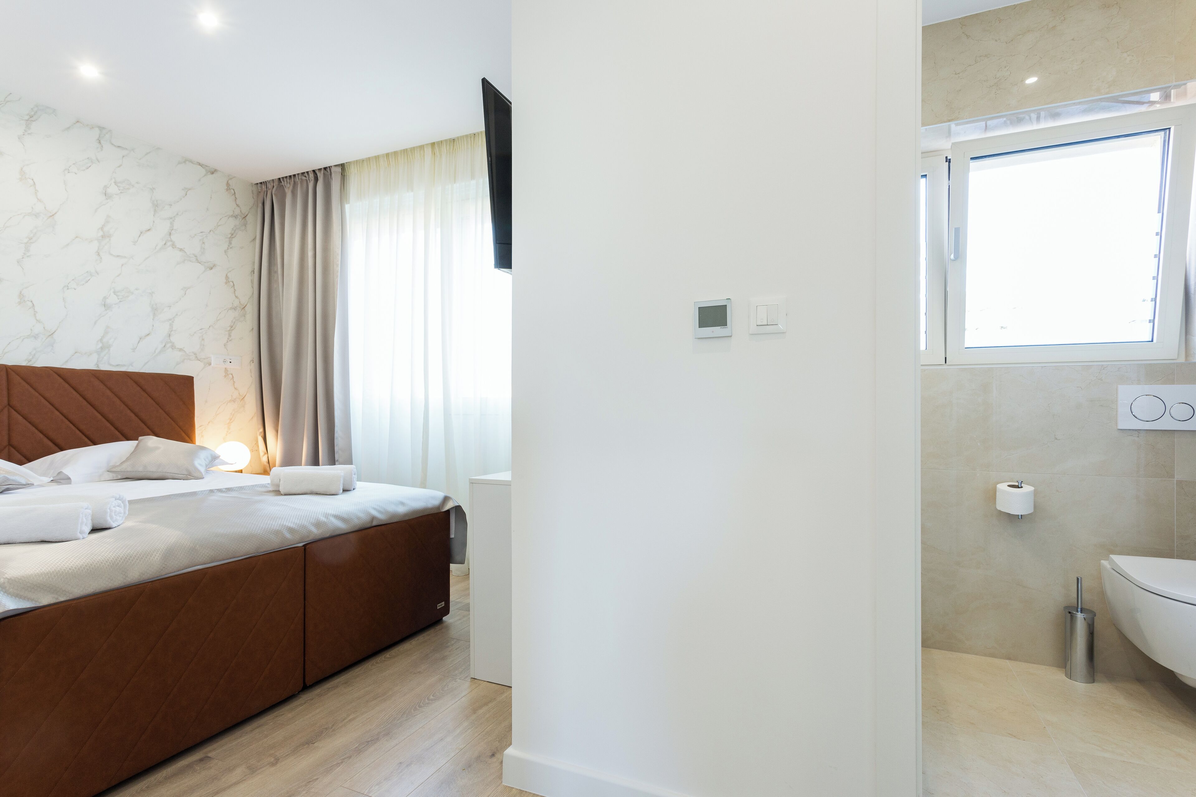 Une chambre d’hôtel moderne dotée d’un grand lit, d’une table de chevet, d’un téléviseur à écran plat et d’une salle de bain avec des toilettes et un lavabo.