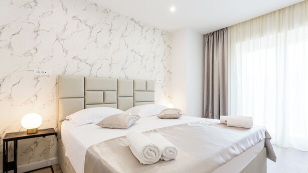 A modern hotel room with a marble-patterned wall, a large bed with a headboard, and a nightstand with a lamp. - Shine of Life Luxury Rooms (Split)