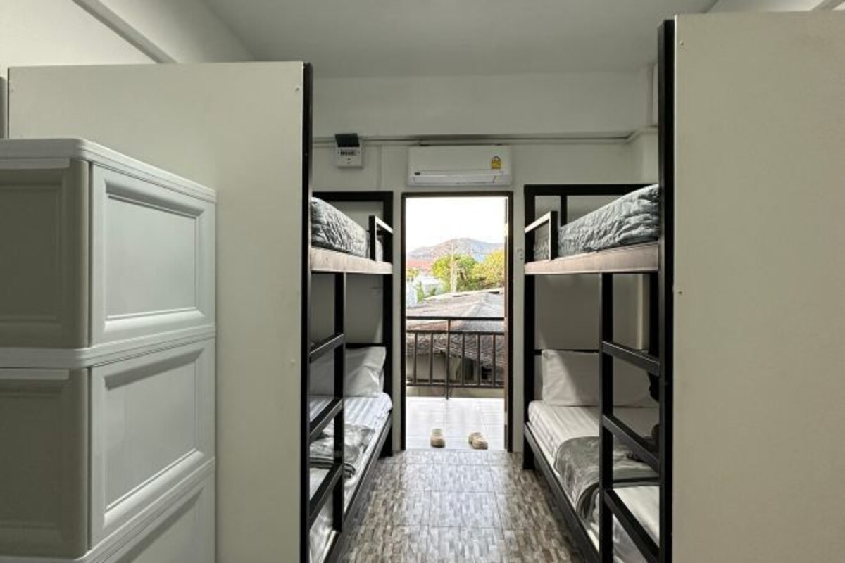 A dormitory room with bunk beds, a small table, and a window with a view of the outdoors.