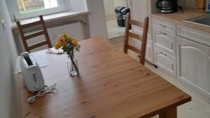Una cuina amb taula de fusta, cadira, cafetera i paperera.