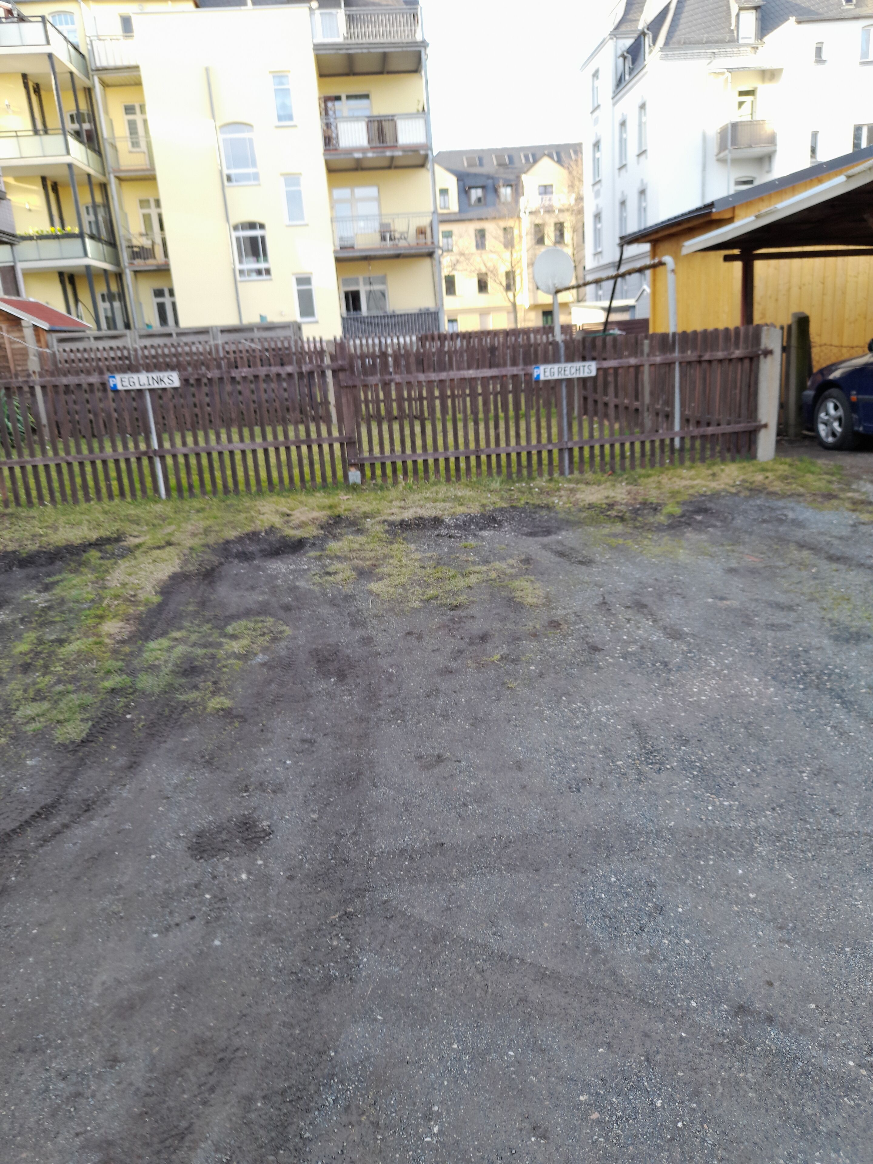 Een omheind buitengebied met een grindoppervlak, omringd door meerhoog gebouwen met balkons.