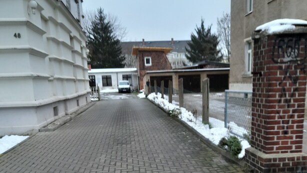 Un camí pavimentat que condueix a un edifici amb façana de maó i una paret exterior blanca.