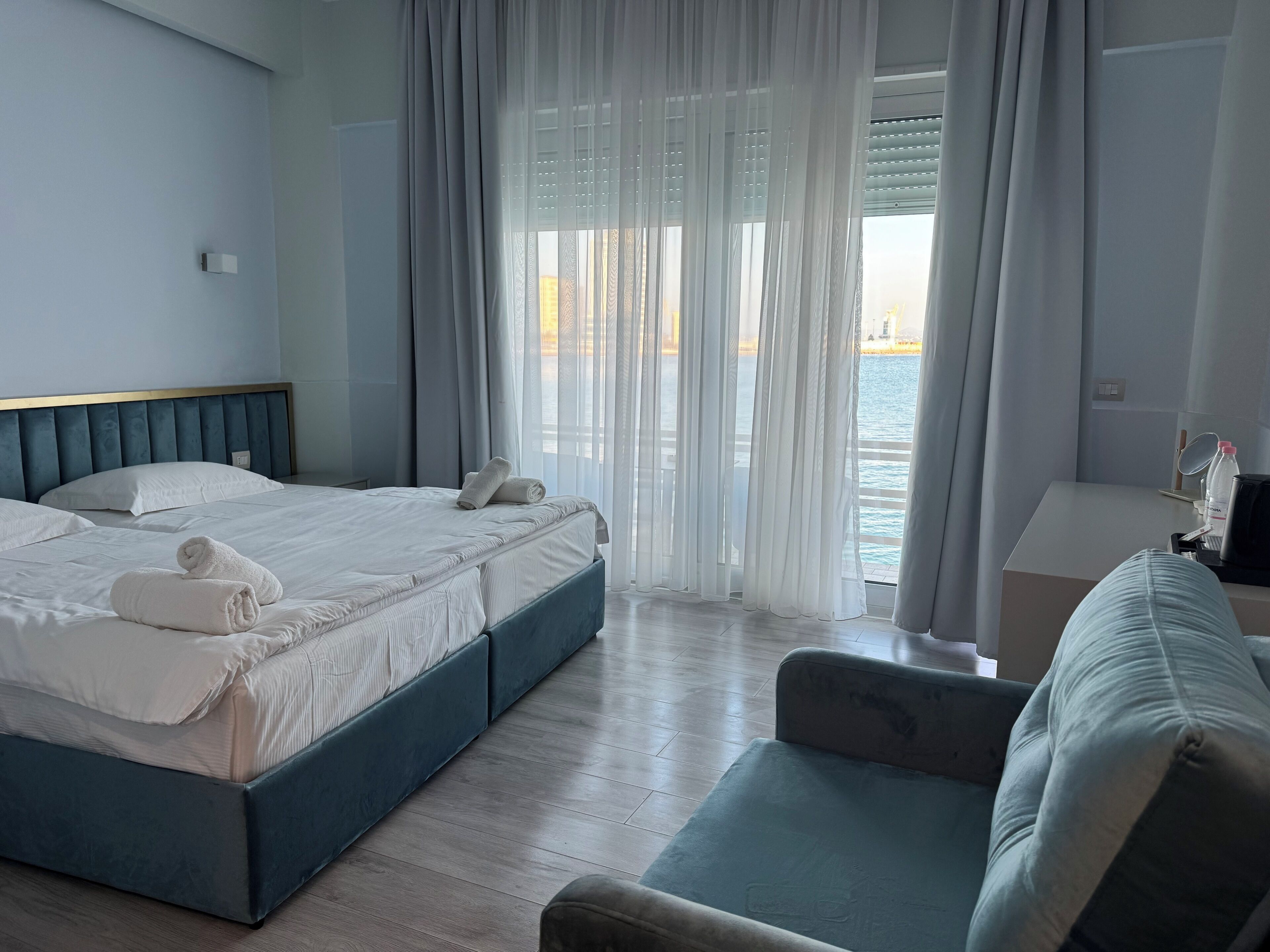 A hotel room with a bed, a sofa, a small table, and a view of the sea.