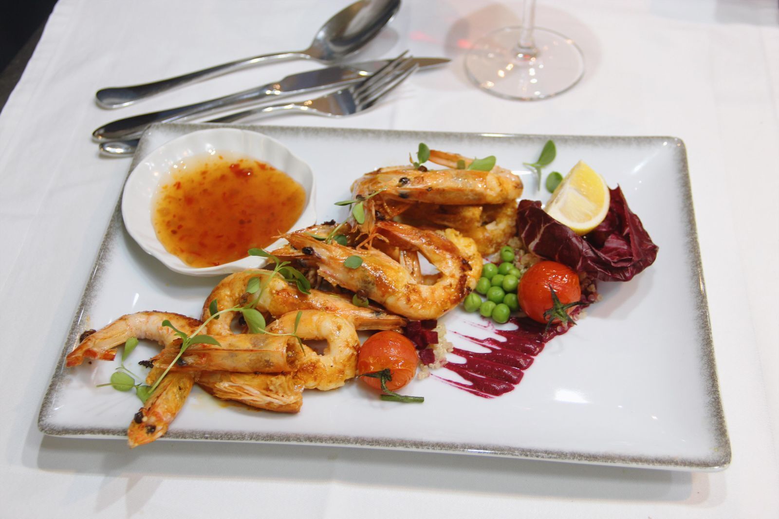 A plate of grilled shrimp with vegetables and a side of sauce.
