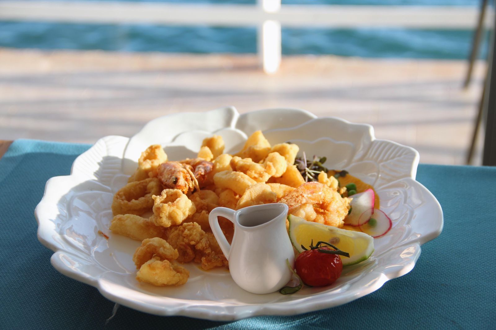 Un piatto di pesce fritto con una piccola brocca di salsa e una fetta di lime su un tavolo vista mare.