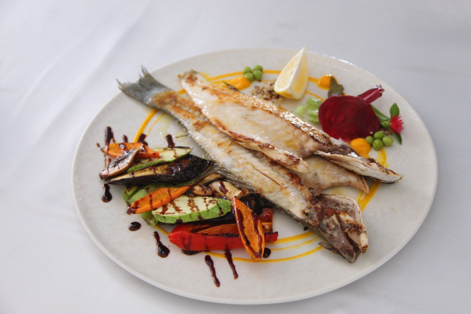 Ein Teller mit gegrilltem Fisch, Gemüse und einer Zitronenscheibe.