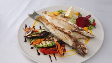 Ein Teller mit gegrilltem Fisch, Gemüse und einer Zitronenscheibe.