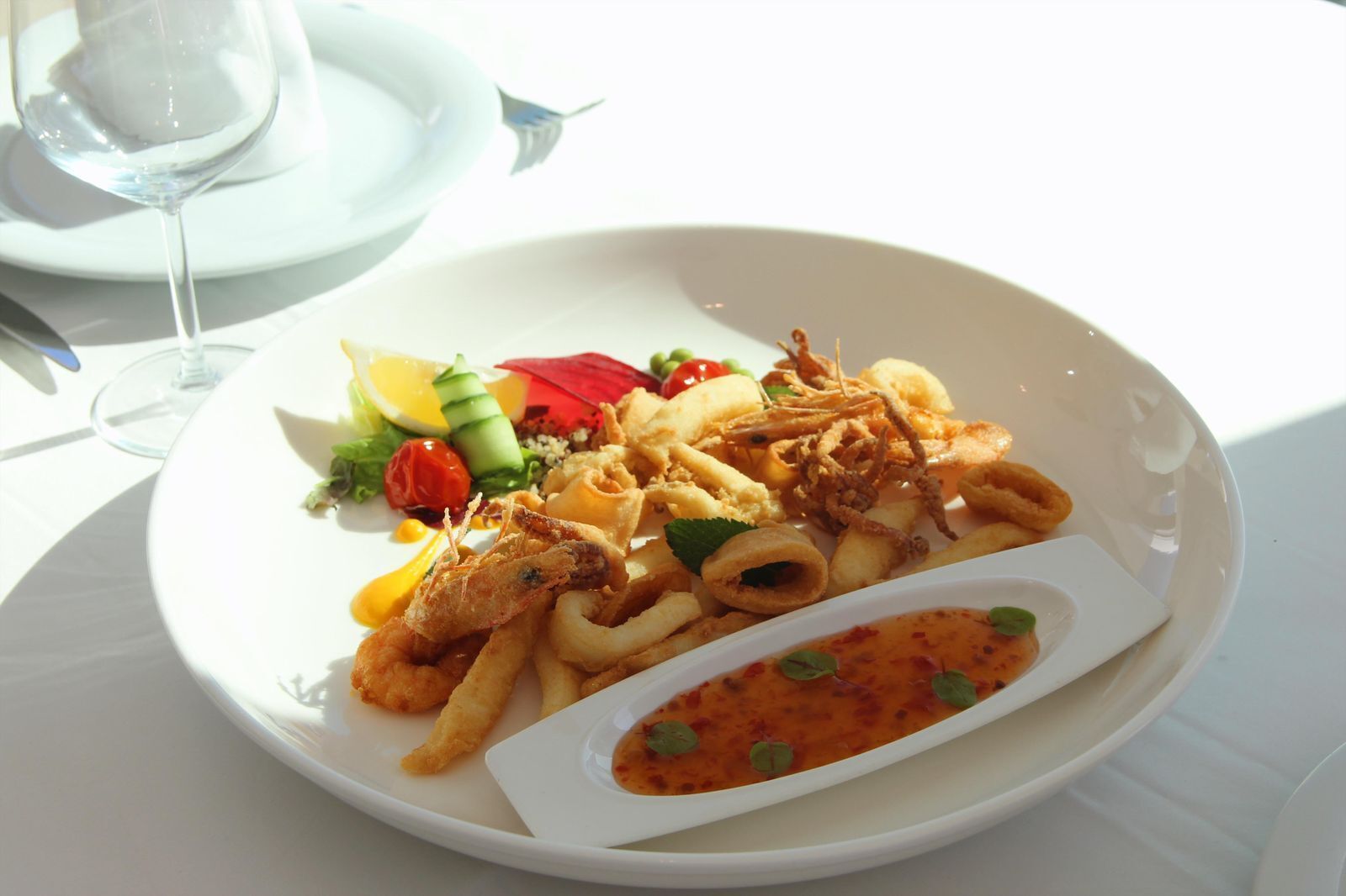 A plate of seafood, including fried calamari and shrimp, with a side of vegetables and a small bowl of sauce.