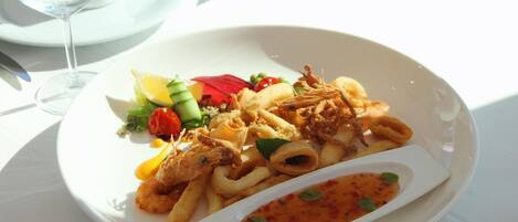 A plate of seafood, including fried calamari and shrimp, with a side of vegetables and a small bowl of sauce.
