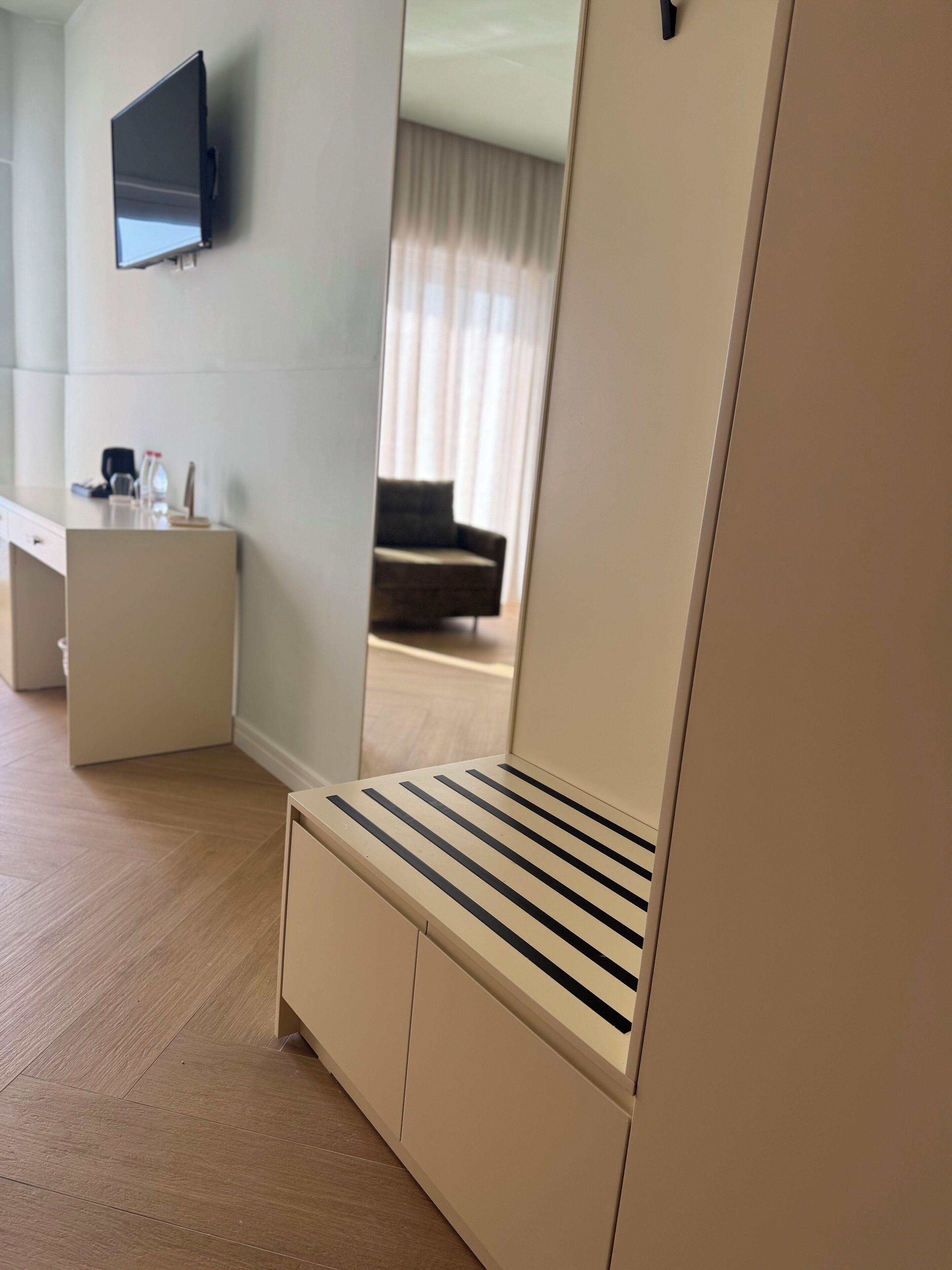 A modern hotel room with a flat-screen TV mounted on the wall, a wooden floor, a sofa, and a small desk with a chair.