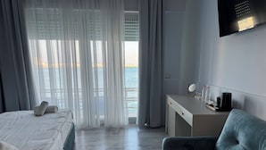 A hotel room with a bed, a desk, a chair, a TV, and a view of the sea. - Ventus Harbor Hotel (Durrës)