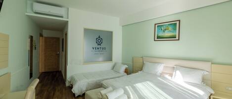 A hotel room with two beds, a wooden door, a framed sign, and a painting on the wall.