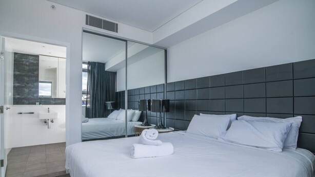 A modern hotel room with a large bed, a bedside table, a mirror, a bathroom with a sink, and a shower area. - free parking lovely 2 bds  in heart of chatswood (Chatswood)