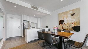 A modern kitchen with white cabinets, a central island, and a dining area with a wooden table and black chairs. - free parking lovely 2 bds  in heart of chatswood (Chatswood)