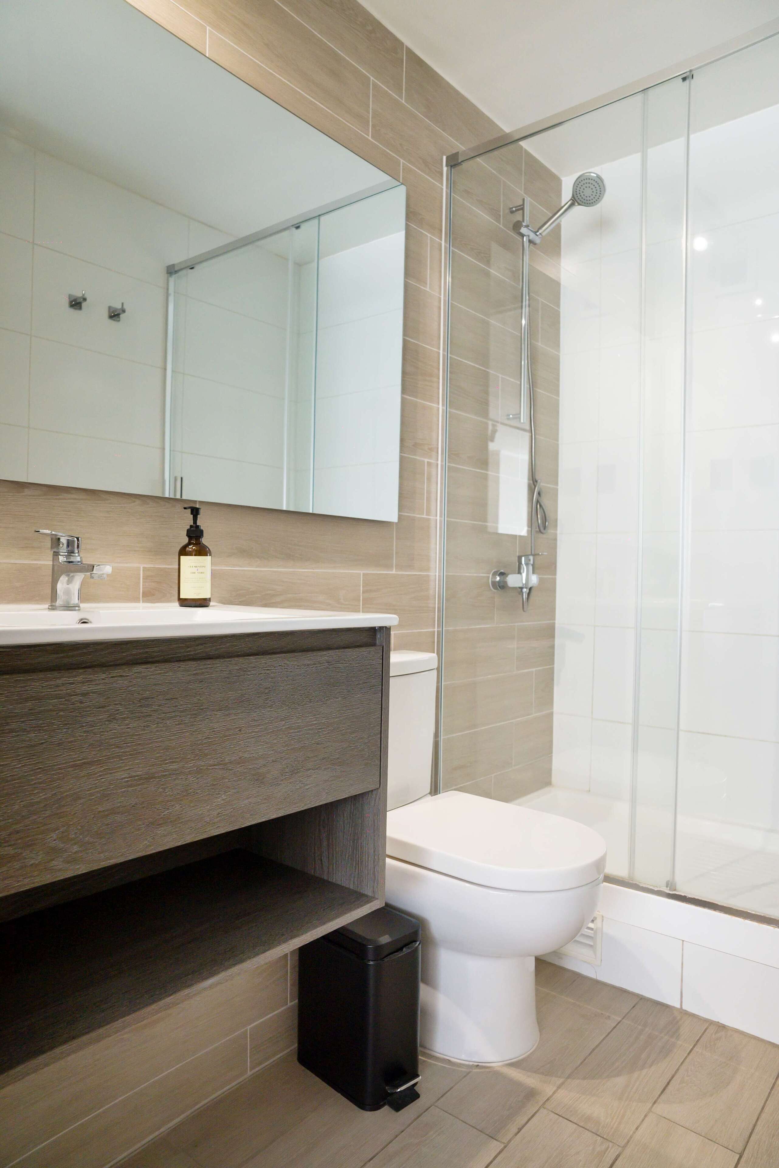 Une salle de bain moderne avec une douche à parois de verre, des toilettes blanches et un meuble-lavabo doté d’un miroir et d’un distributeur de savon.