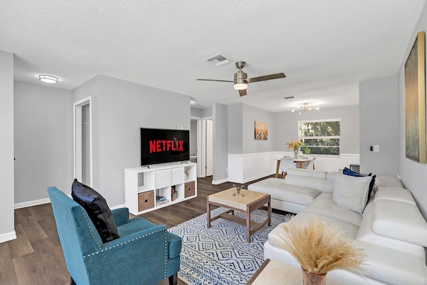 Modern living room with a white sectional sofa, blue armchair, and a television with streaming service access.