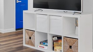 A room with a large flat-screen TV on a white stand, a blue door, and storage units with board games. - Backyard BBQ home - Blue Spring to Daytona (Orange City)