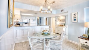 Un coin repas avec une table en verre entourée de chaises en osier, un lustre et un vase contenant des objets décoratifs posé sur la table.