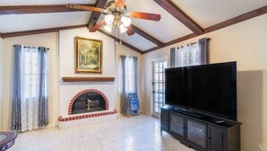 A living room with a fireplace, a large flat-screen TV, and a ceiling fan. - Spacious 4BR with Private Pool, Near Six Flags (San Antonio)