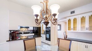 A modern kitchen with white cabinets, a glass dining table, and a chandelier. - Spacious 4BR with Private Pool, Near Six Flags (San Antonio)