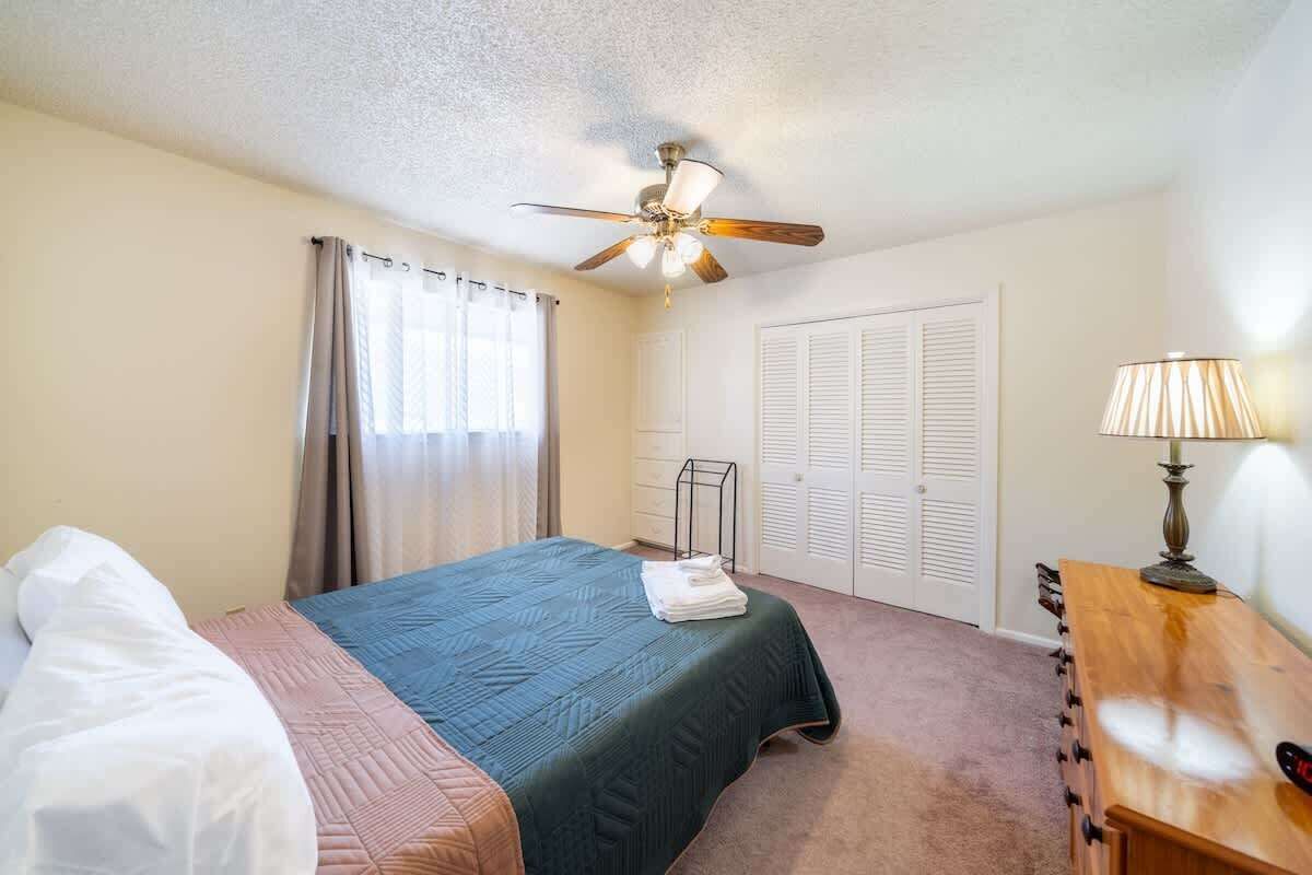 Une chambre à coucher avec un lit, un ventilateur de plafond, un bureau avec une lampe et un placard.