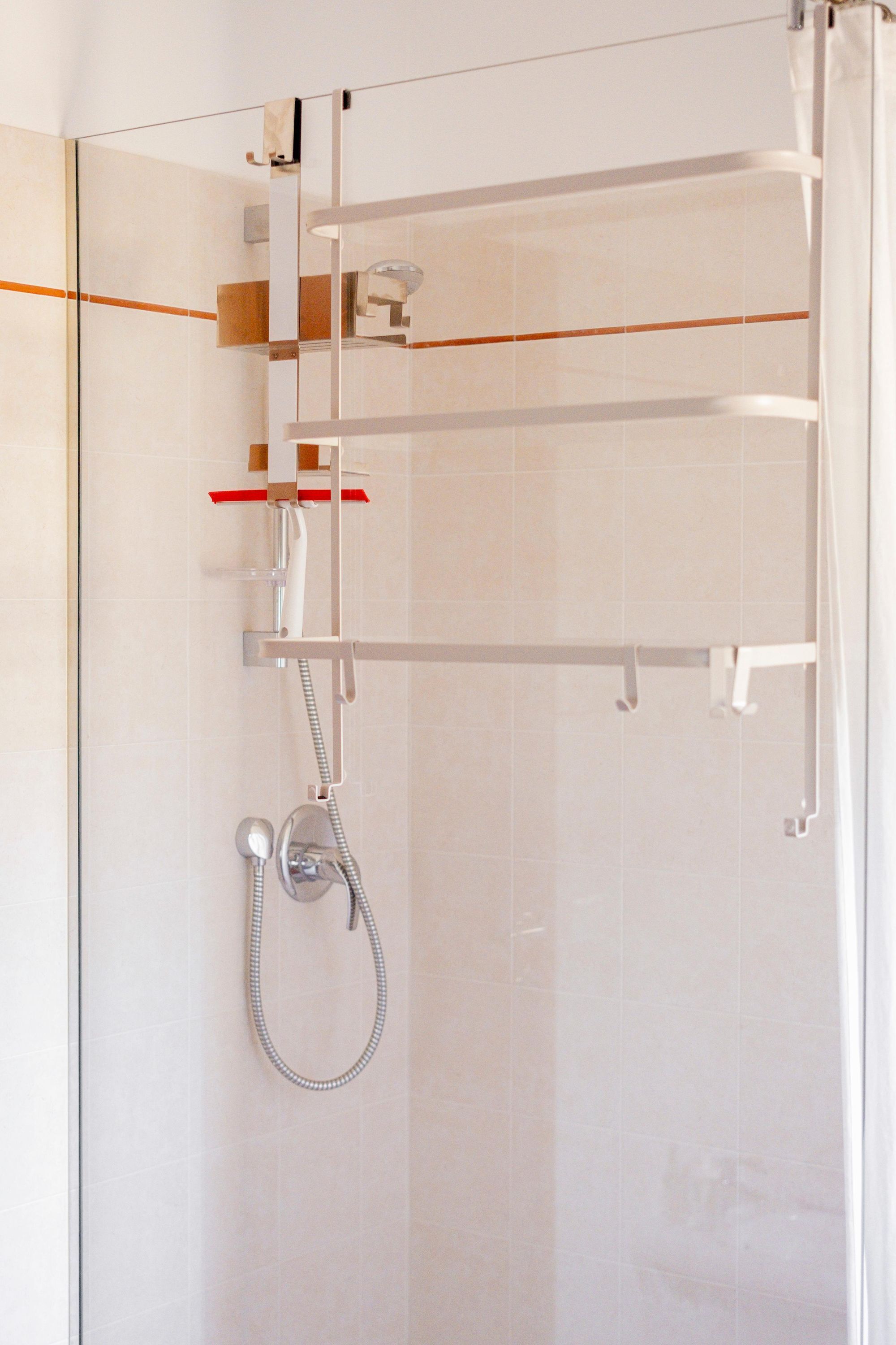 Une douche fermée par des parois en verre, dotée d’un pommeau de douche à main et d’un panneau de commande fixé au mur.