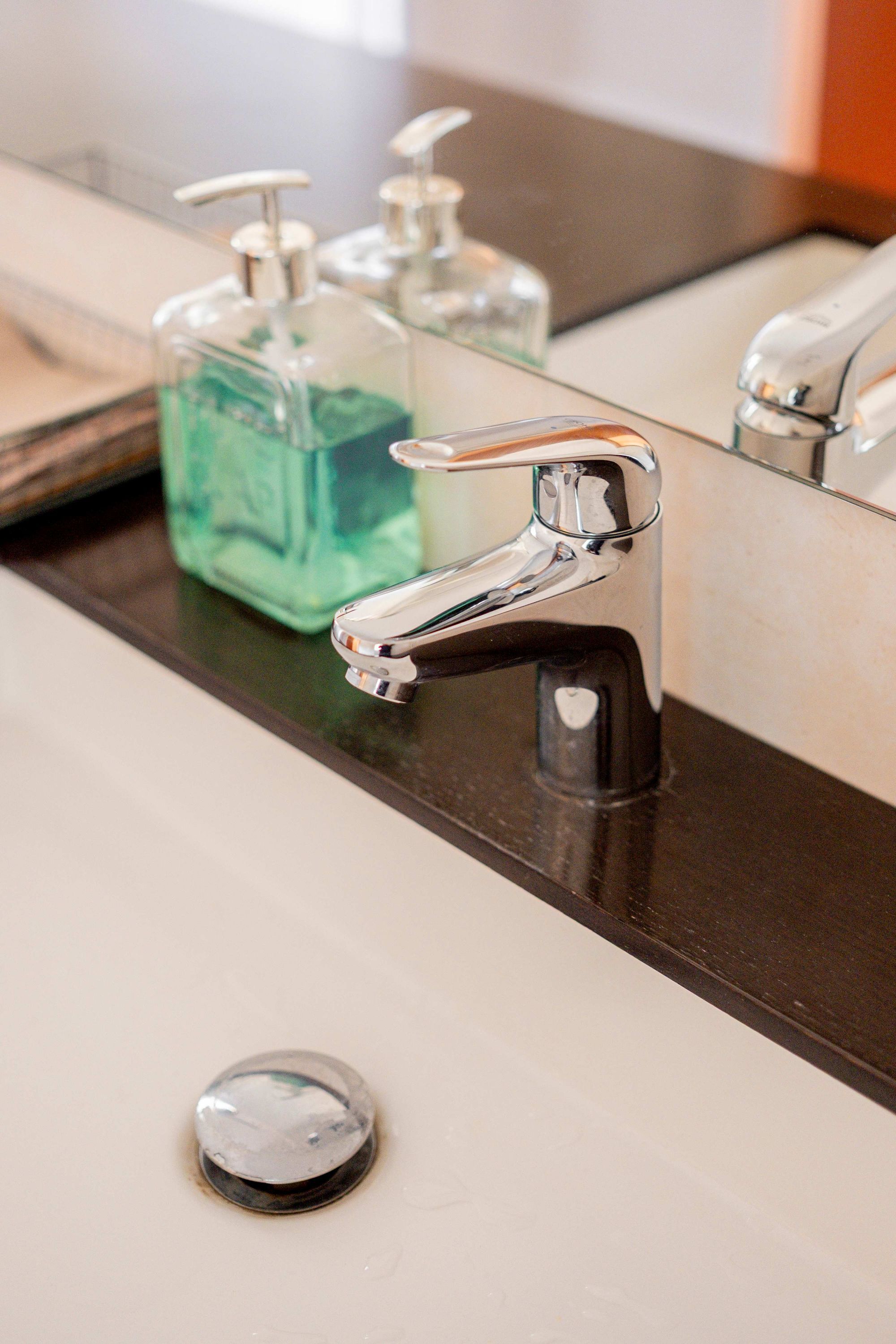 Ein Waschbecken mit einem Chrom-Wasserhahn, einer Seifenspender und einer Glas-Seifenflasche.