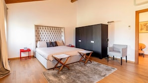 A bedroom with a large bed, a dark wardrobe, a small red table, and a grey armchair.
