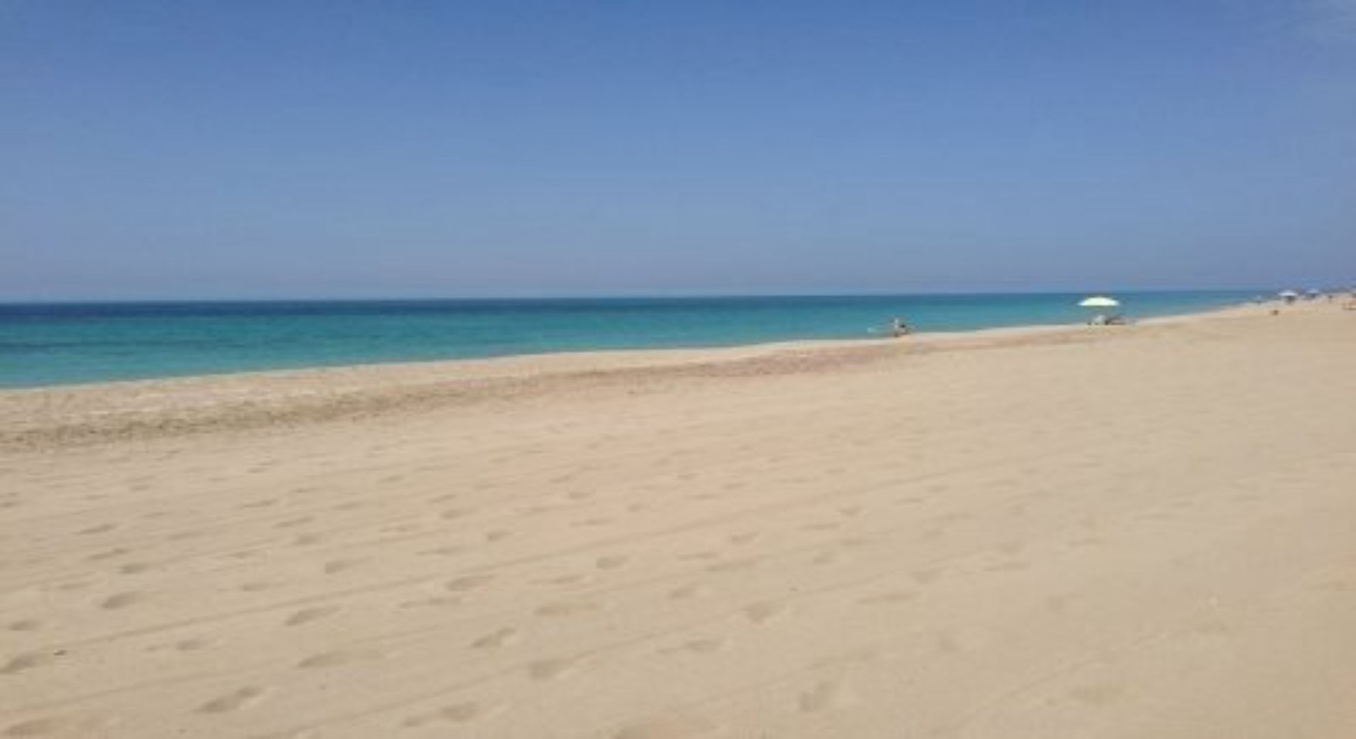 Une vaste plage de sable fin, sous un ciel dégagé.