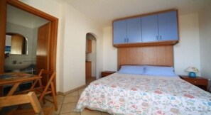 Een slaapkamer met een bed, houten hoofdbord, bureau met stoel, spiegel en garderobe.
