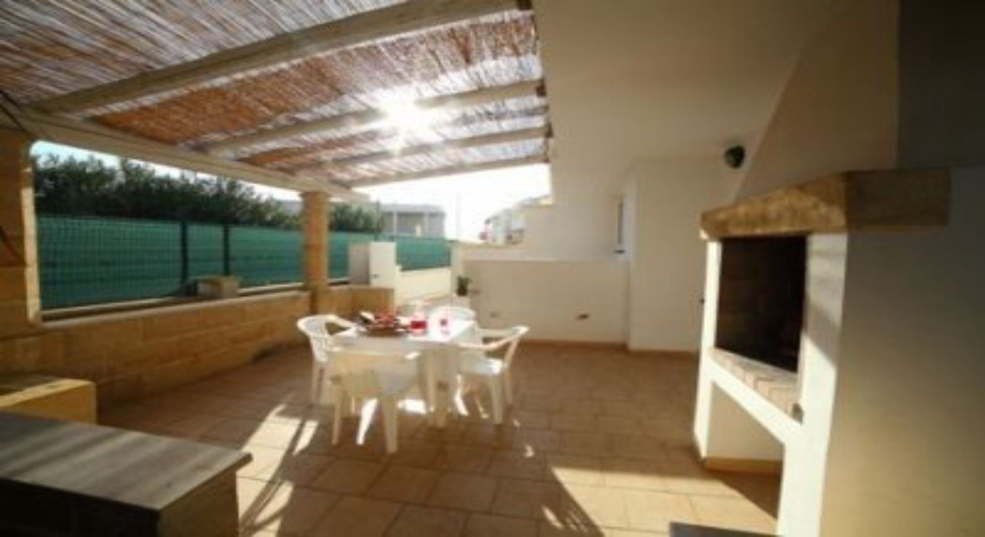 Una veranda esterna con tavolo e sedie, un muro in mattoni e un televisore.