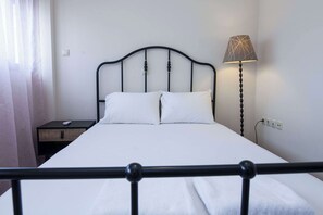 Ein ordentlich bezogenes Bett mit weißen Leinen, einem schwarzen Metall-Kopfstück, einem Nachttisch mit Fernbedienung und einer Lampe.