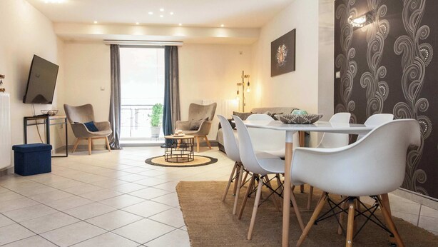 A modern living room with a dining area, a TV, and a large window. - Elegant Spacious 2Bd Apt with Balcony in Petralona (Athina)