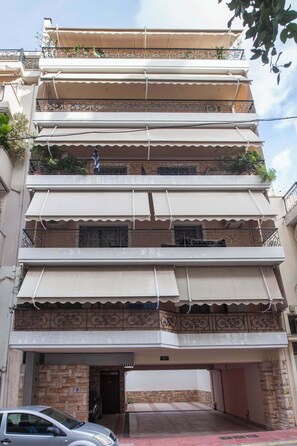 Ein mehrstöckiges Wohnhaus mit Balkonen, Markisen und einem Parkplatz.