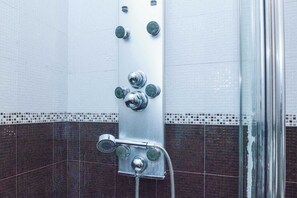 A shower with multiple heads and a handheld showerhead, tiled walls, and a glass shower enclosure.