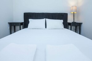 Un lit bien fait, avec du linge de lit blanc, deux tables de chevet et une lampe sur l’une des tables.