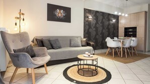 A modern living room with a grey sofa, a round coffee table, and a dining area with a white table and chairs. - Elegant Spacious 2Bd Apt with Balcony in Petralona (Athina)
