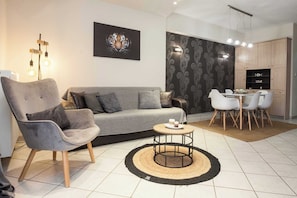 Ein modernes Wohnzimmer mit einer grauen Couch, einem runden Couchtisch und einem Essbereich mit weißem Tisch und Stühlen.