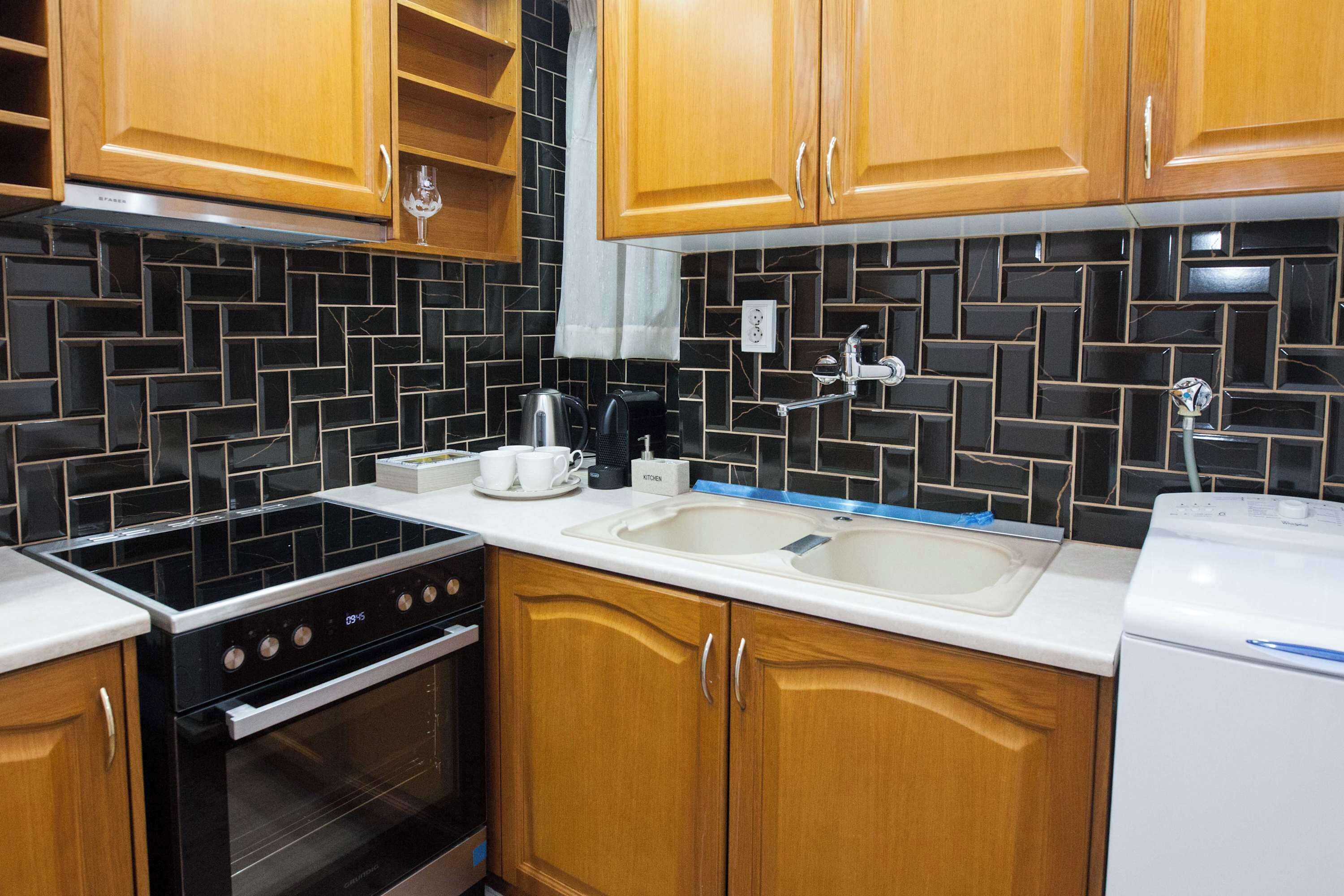 A kitchen with wooden cabinets, a black tiled backsplash, a stove, a sink, and a washing machine.