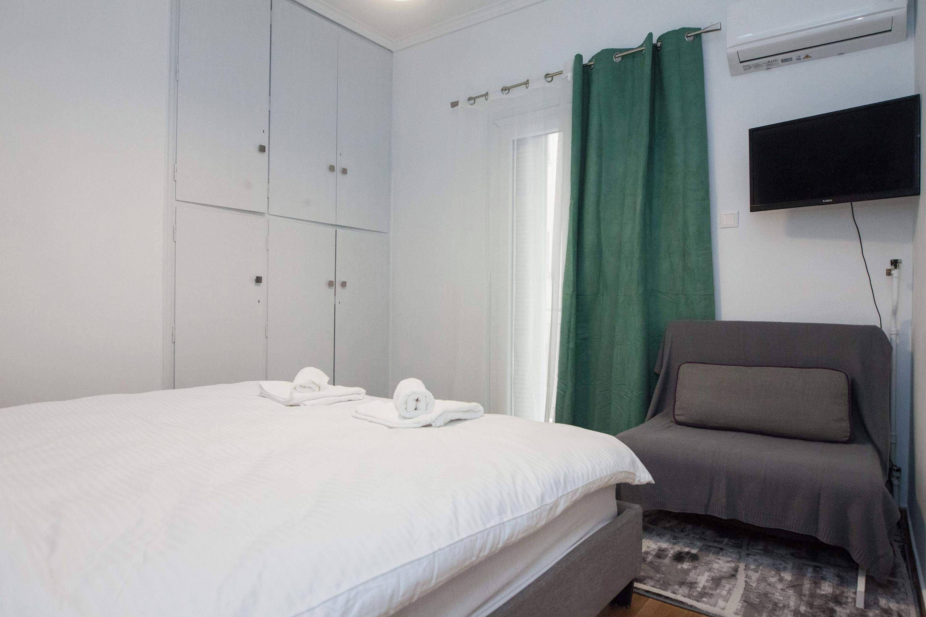 A hotel room with a bed, a chair, a television, and an air conditioning unit.