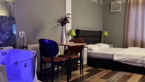 A hotel room with a bed, a desk with a chair, a small table with a vase, a massage chair, and a wooden floor. - vera pansıyon (Istanbul)