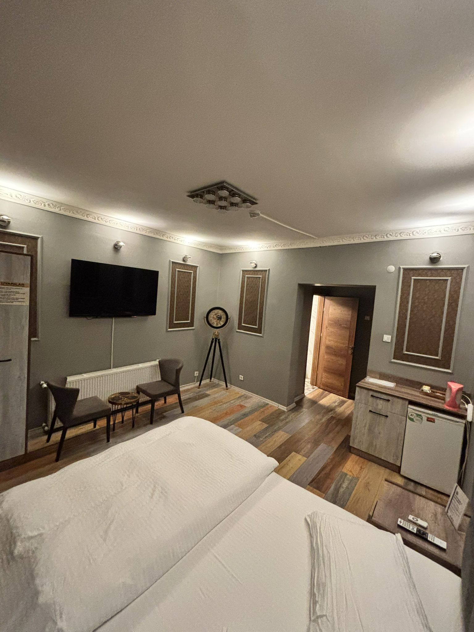 Habitación de hotel con una cama grande, un escritorio, una silla, un televisor y una pequeña cocina.