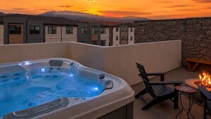 A hot tub on a rooftop terrace with a sunset view, stone wall, and outdoor seating. - The Desert Haven l Rooftop Hot Tub & Game Room (Hurricane)