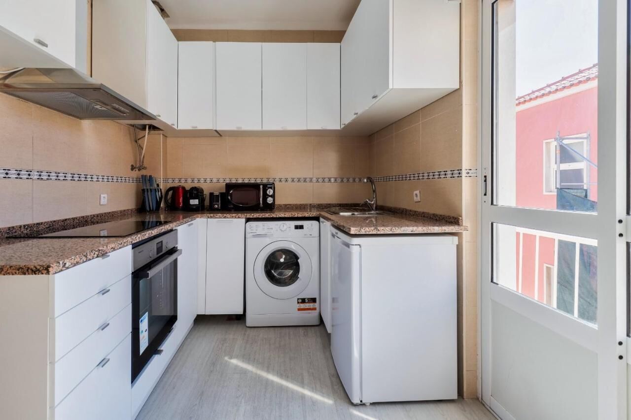 A compact kitchen with white cabinets, a microwave, a washing machine, and a sink.